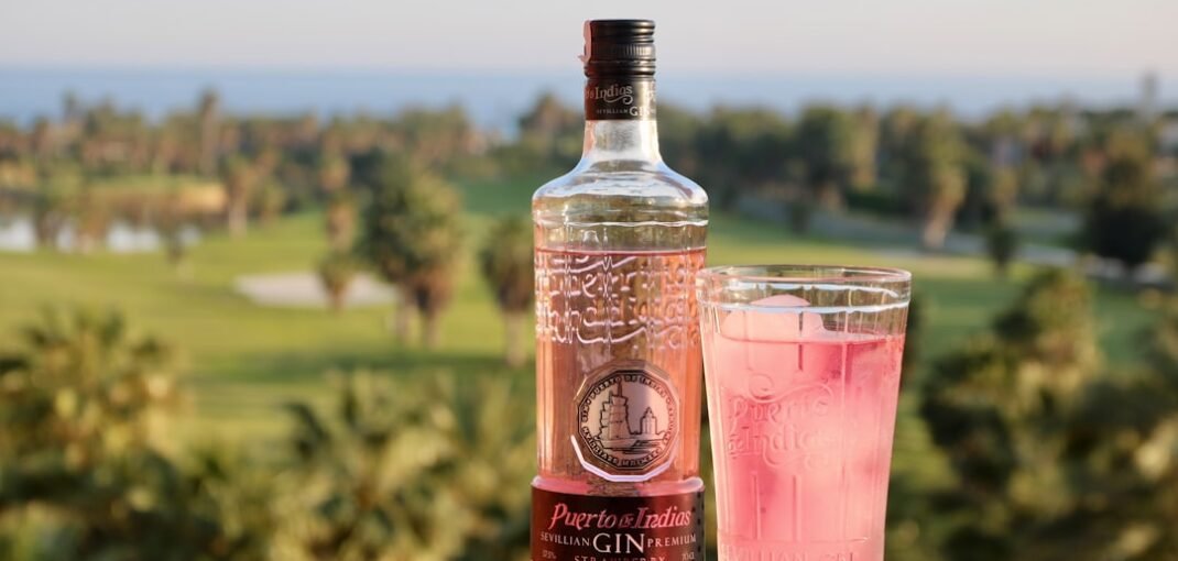 A pink gin cocktail in a coupe glass with rose petals and ice, showcasing the delicate blush colour of pink gin