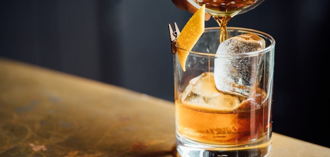 A glass of amber whisky beside a bottle on a wooden surface, ideal for browsing whisky online in New Zealand winter