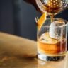 A glass of single malt scotch whisky on a dark wooden surface with a bottle in the background