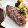 A glass of red wine and a whisky beside a perfectly seared steak on a wooden board, whisky wine gin steak pairings
