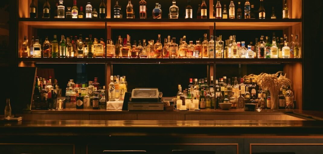 A home bar whisky collection with several bottles of Scotch, bourbon and Irish whisky arranged on a wooden shelf