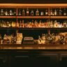 A home bar whisky collection with several bottles of Scotch, bourbon and Irish whisky arranged on a wooden shelf