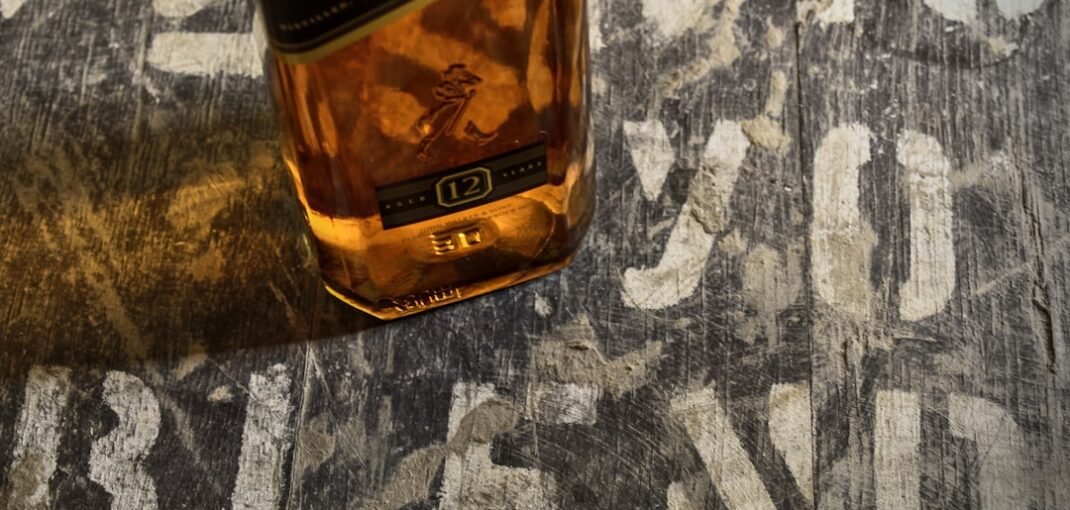 Bottle of Johnnie Walker Black Label 700mL on a dark wooden surface with a glass of whisky