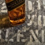 Bottle of Johnnie Walker Black Label 700mL on a dark wooden surface with a glass of whisky